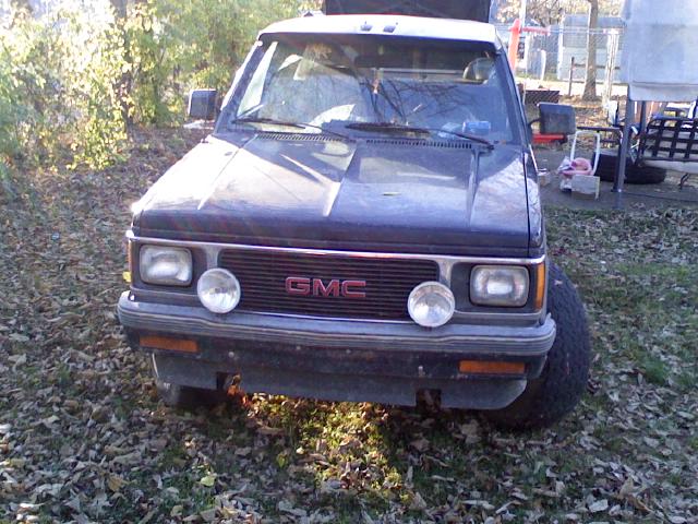 Weathered dark blue GMC compact pickup, front view on leaf-covered grass