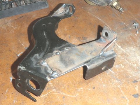 1994 Ford Bronco - A modified metal bracket, likely for a vehicle, rests on a workbench with tools nearby.