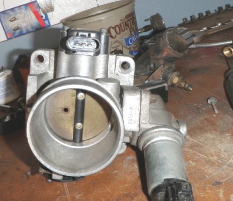 1994 Ford Bronco - A close-up view of a throttle body assembly, likely for an automotive engine, resting on a workbench.