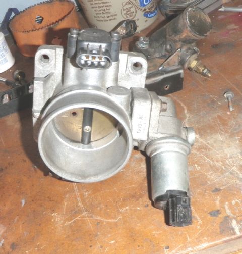 1994 Ford Bronco - A throttle body assembly is shown on a workbench, detached from a vehicle.
