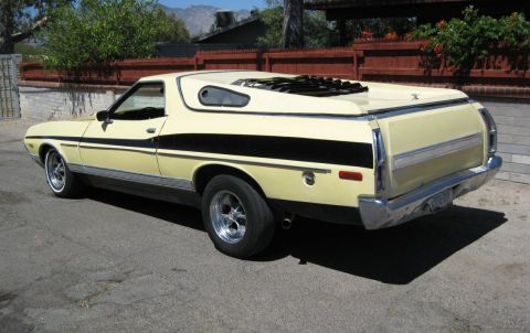 1972 Ford Ranchero - Rear three-quarter view of a yellow 1972-vintage Ford Ranchero car-pickup with black side stripes, hood scoop and chrome wheels.