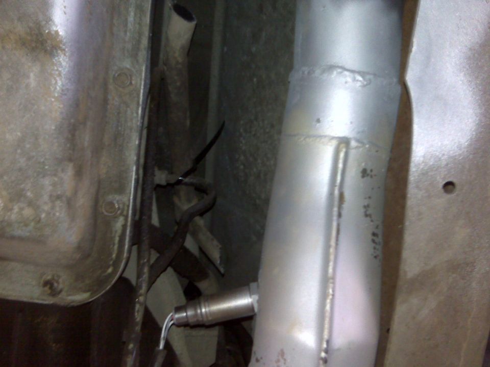 Close-up of an exhaust pipe with an oxygen sensor attached, showing metal components and wiring