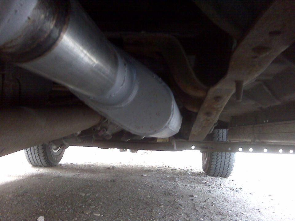 Underside view of a pickup truck's exhaust system and frame, showing the rear tire