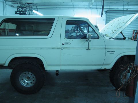1986 Ford Bronco - Side view of a white 1986 Ford Bronco with its hood open, parked indoors.