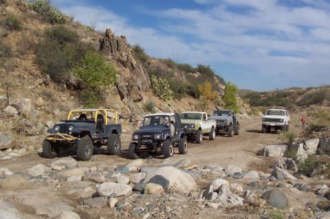 1981 Ford F-150 - A convoy of off-road vehicles navigates a challenging rocky trail under a blue sky.
