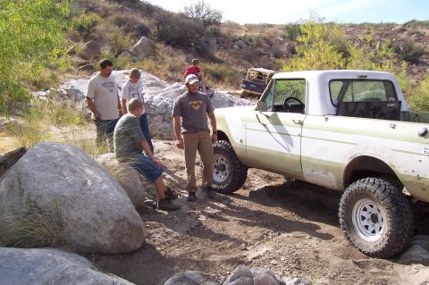 1981 Ford F-150 - People gathered around a pickup truck on a rough, rocky trail with another vehicle in the distance.