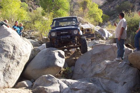 1981 Ford F-150 - A Suzuki Samurai is driven over large rocks in a outdoor setting, with several people observing the off-road action.