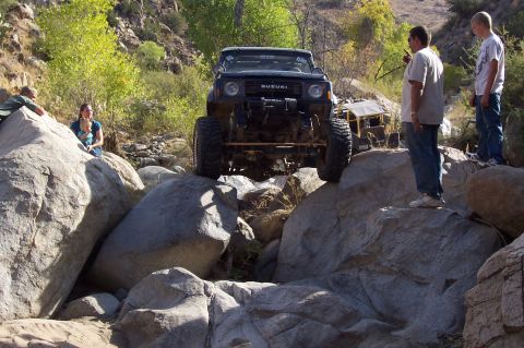 1981 Ford F-150 - Suzuki Samurai navigating a rocky trail with spectators observing the action.