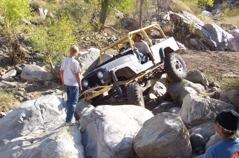 1981 Ford F-150 - A modified Jeep CJ-7 navigates a rocky off-road trail with onlookers.