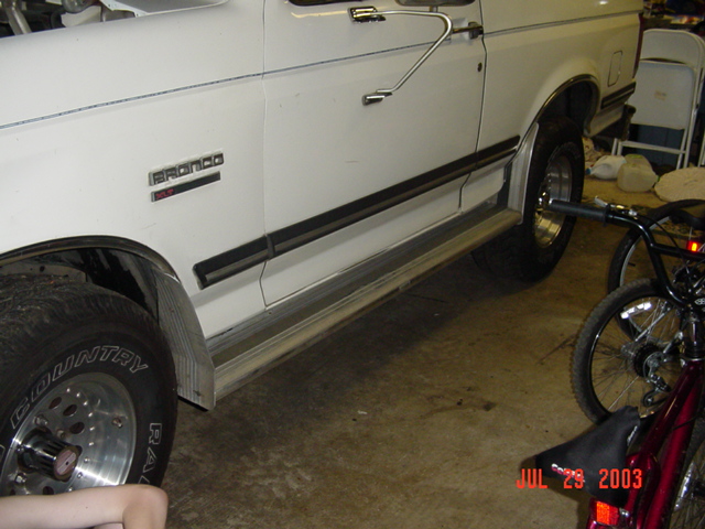 White Ford Bronco side profile in a garage with chrome wheels and rocker trim