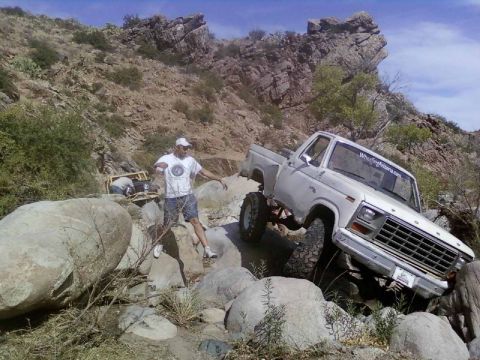 1981 Ford F-150 - A white pickup truck is shown off-roading on a rocky, mountainous trail with a man observing.