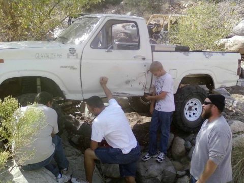 1981 Ford F-150 - A white Ford F-150 pickup truck with off-road tires is stuck on a rocky incline, with several people around it.