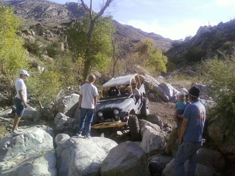 1981 Ford F-150 - A group of people observe a Jeep as it traverses a difficult, rocky path in a mountainous, arid environment.