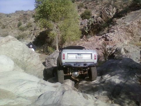 1981 Ford F-150 - An off-road vehicle navigates a challenging rocky terrain under a clear sky.