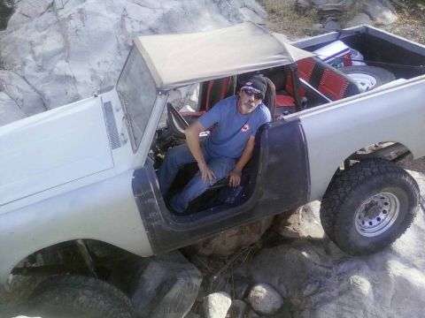 1981 Ford F-150 - A man sits in a white off-road truck navigating rocky terrain.