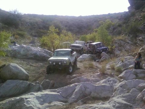 1981 Ford F-150 - Several trucks are seen off-roading on a challenging, rocky path in a hilly, arid landscape.
