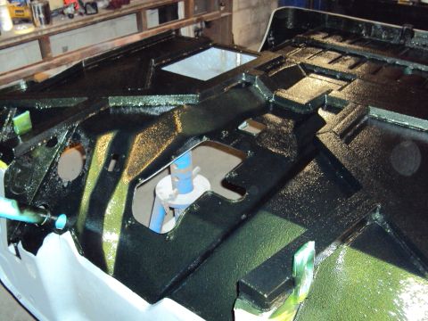 1948 Jeep Wrangler - The chassis of a vehicle is being painted black, showing intricate structural details and some green undercoating.