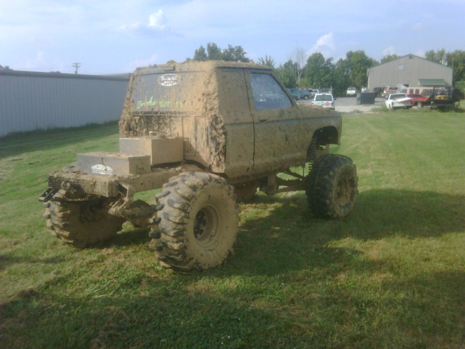 Lifted compact pickup caked in dried mud on mud-terrain tires parked on grass