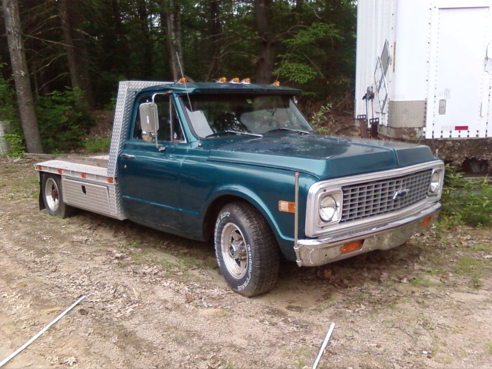 Teal flatbed truck with a chrome grille and diamond plate bed, parked on a dirt lot