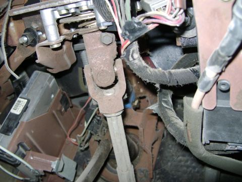 1998 Ford Crown Victoria - Close-up view of the steering column universal joint and associated wiring harness components located under the dashboard.