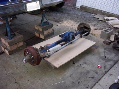 1980 Ford Bronco - Front axle assembly removed from a vehicle, resting on a wooden board with shocks and steering linkage visible.