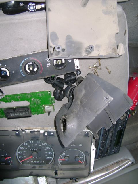 1998 Ford Crown Victoria - Disassembled interior car parts, including the instrument cluster and climate control panel, are spread out on a surface.