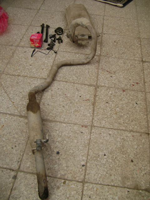 1998 Ford Crown Victoria - A used exhaust system part is laid out on a tiled floor with accompanying hardware.