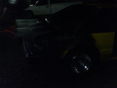 1992 Ford Mustang - A dark-colored car is partially visible with a yellow rear panel and a chrome wheel, parked near a white truck.