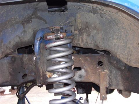 1980 Ford Bronco - Close-up of a front suspension coil spring and blue shock mount, with visible rust and wear.