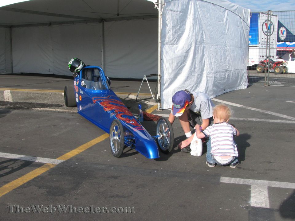 blue dragster with orange flame graphics, man and kid nearby