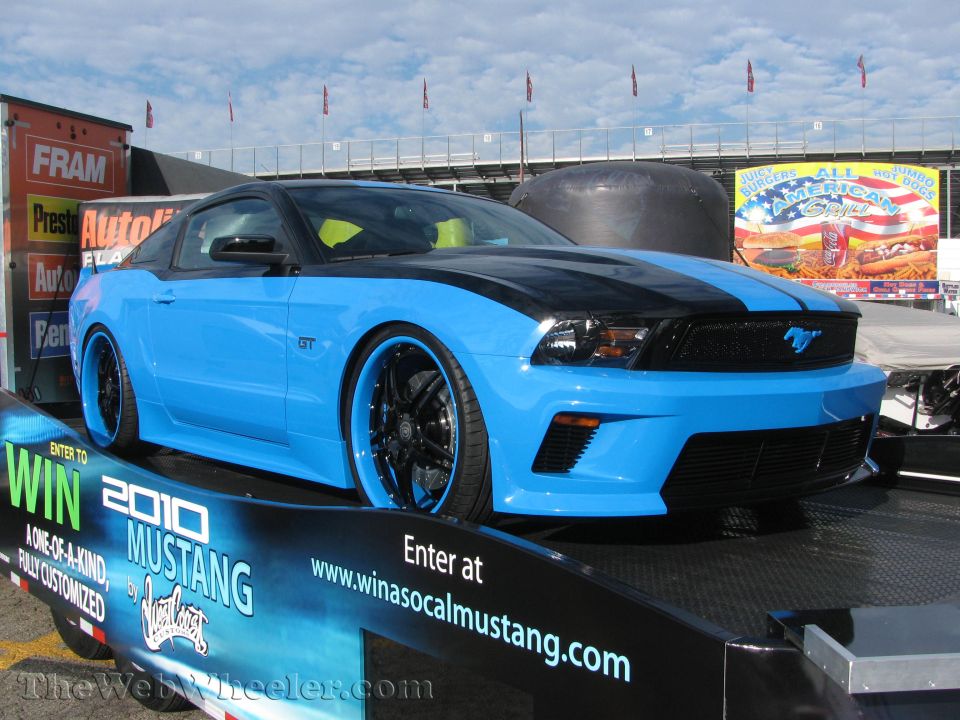 Blue 2010 Ford Mustang GT with black racing stripes and custom rims on a trailer