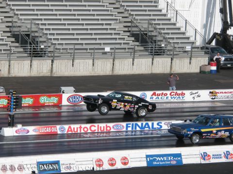 1968 Ford Mustang - Two cars compete on a drag strip, with one performing a wheelie as it accelerates down the track.