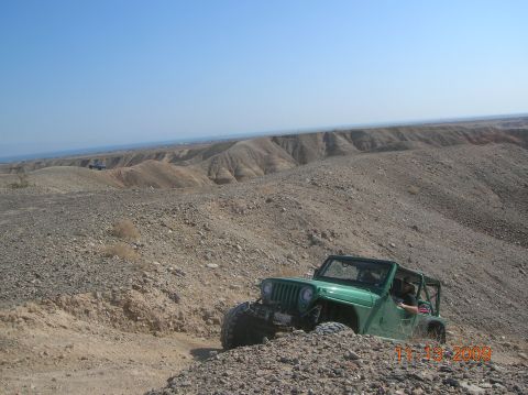 1985 Ford Bronco - A green Jeep Wrangler navigates a steep, rocky incline in a desert landscape.
