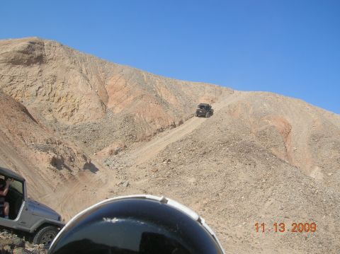 1985 Ford Bronco - Two off-road vehicles navigate a challenging desert terrain on a sunny day.