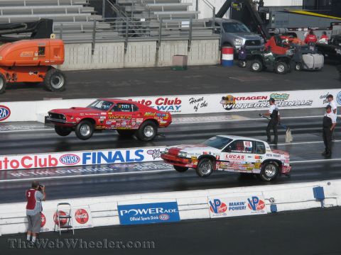 1968 Ford Mustang - Two drag cars compete side-by-side, with their front wheels lifted off the track during a race.