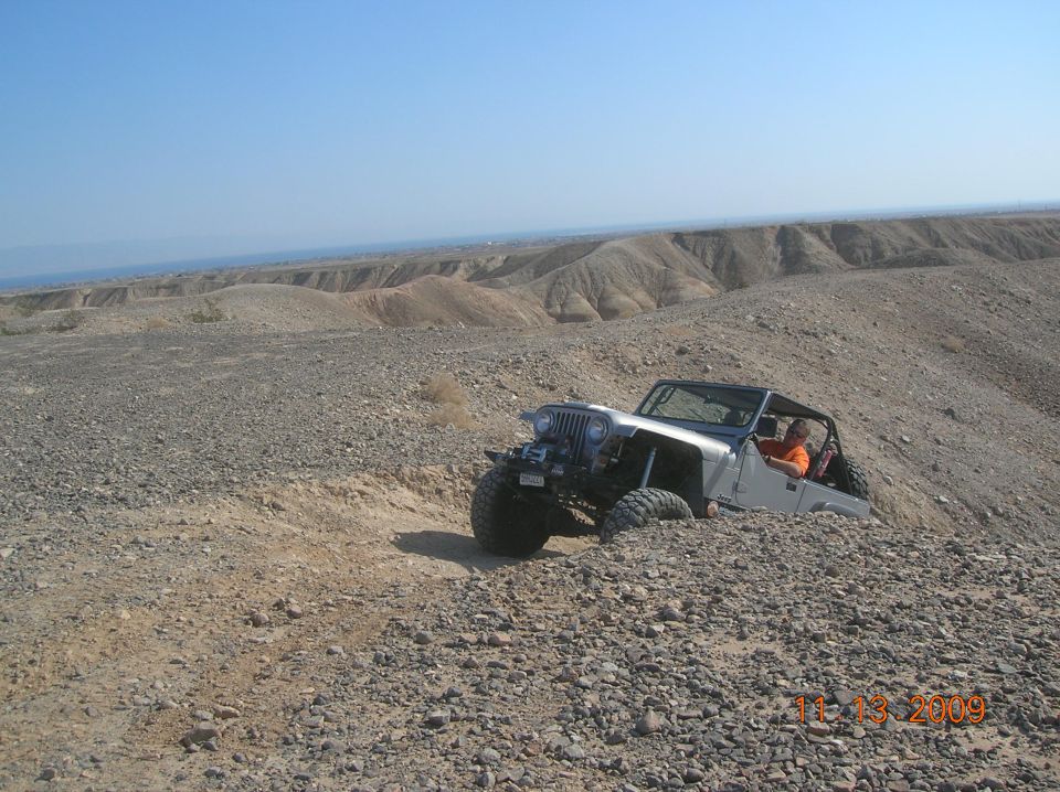 Silver Jeep Wrangler navigating a steep, rocky incline in a desert
