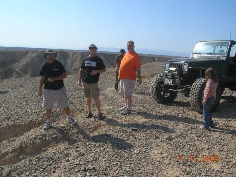 1985 Ford Bronco - A group of people stand near a modified off-road vehicle in a desert landscape.