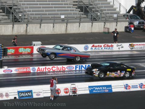 1968 Ford Mustang - A silver 1969 Dodge Charger lifts its front wheels during a drag race against a black car at Auto Club Raceway.