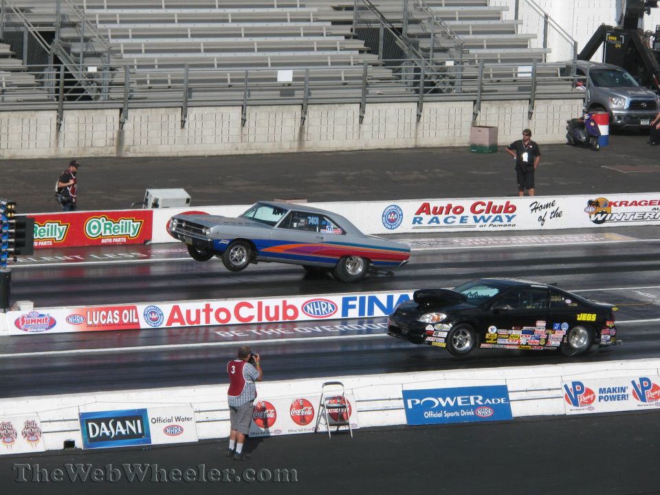 Silver 1969 Dodge Charger drag car with blue and red stripes, front wheels off the ground, racing a black car