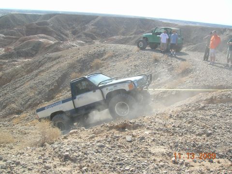1985 Ford Bronco - Two off-road vehicles navigate a steep, rocky terrain on a sunny day.