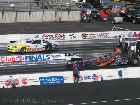 1968 Ford Mustang - Two drag racing cars compete on a track during the NHRA Finals, with spectators and support vehicles in the background.