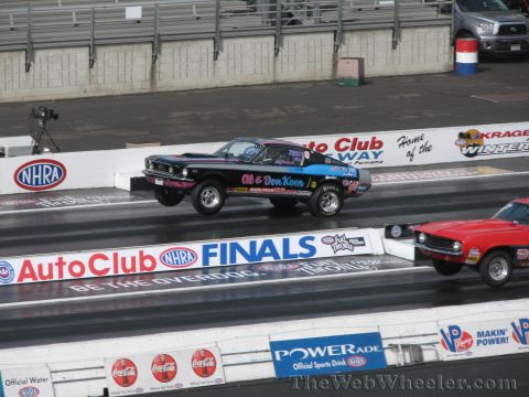 1968 Ford Mustang - Two drag cars compete on a track, with one Mustang lifting its front wheels during acceleration.