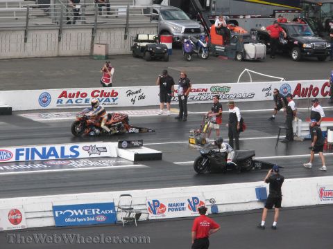 1968 Ford Mustang - Two motorcycles compete at the NHRA Finals, with various support vehicles and spectators in the background.