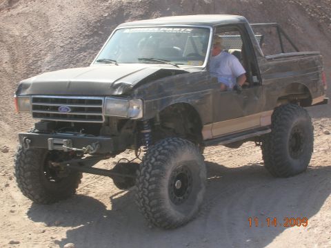 1985 Ford Bronco - This modified 1985 Ford Bronco, seen off-road, features oversized tires, a winch, and a roll cage.