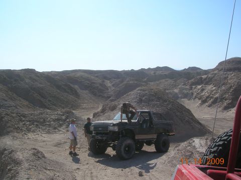 1985 Ford Bronco - Off-road vehicles gathered in a desert landscape under a clear blue sky.