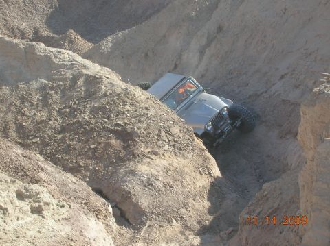 1985 Ford Bronco - A Jeep CJ-5 is shown off-roading in a tight canyon with steep, sandy walls.