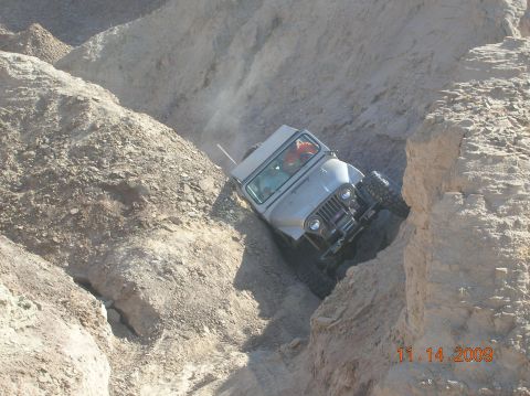 1985 Ford Bronco - A Jeep CJ-7 descends a treacherous, narrow dirt path in a desert canyon.