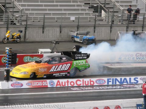 1968 Ford Mustang - A drag racing car performs a burnout on the track, kicking up a cloud of smoke.