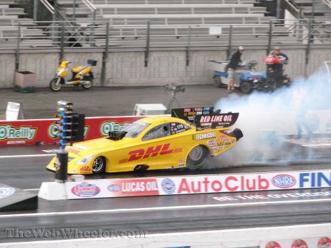 1968 Ford Mustang - A yellow drag racing car with 'DHL' branding speeds down a track, kicking up smoke.