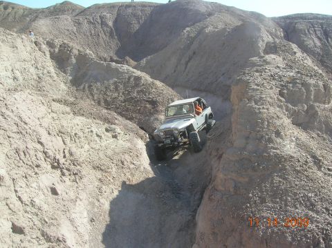 1985 Ford Bronco - A Jeep navigates a challenging off-road trail through a rocky, eroded landscape.